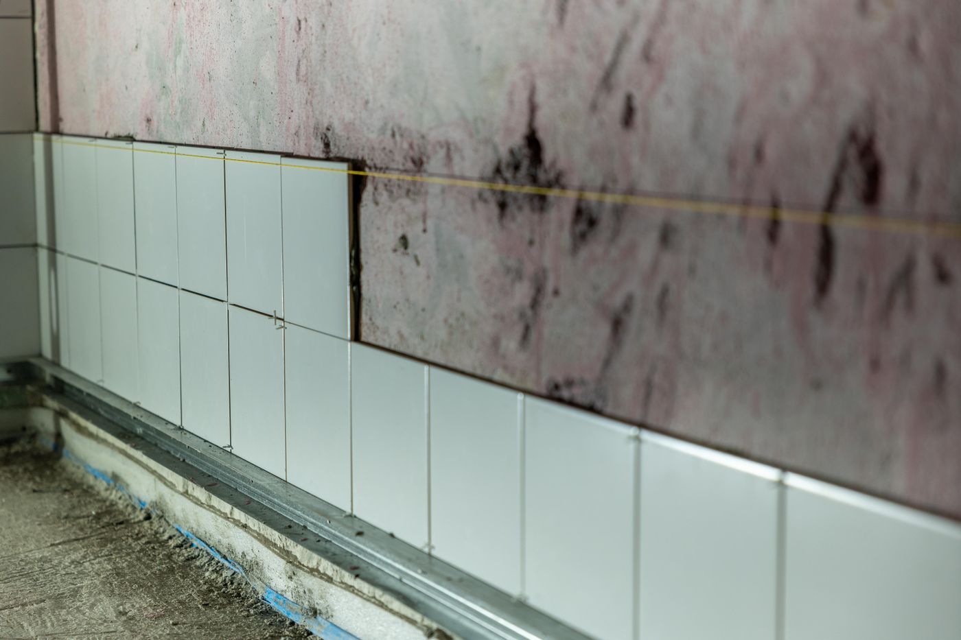 Tegelwand in aanbouw met lichtblauwe tegels en een waterpaslijn